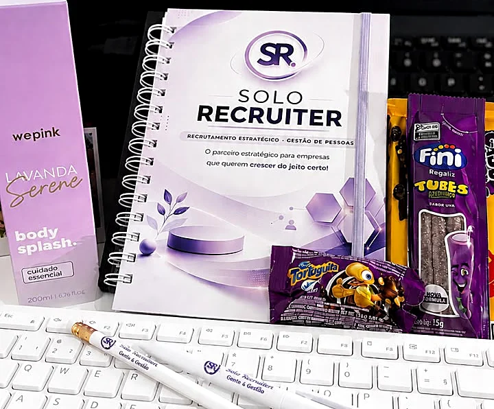 Kit de boas-vindas da Solo Recruiter: caderno com a marca, lápis personalizados, body splash e doces sobre a mesa de trabalho